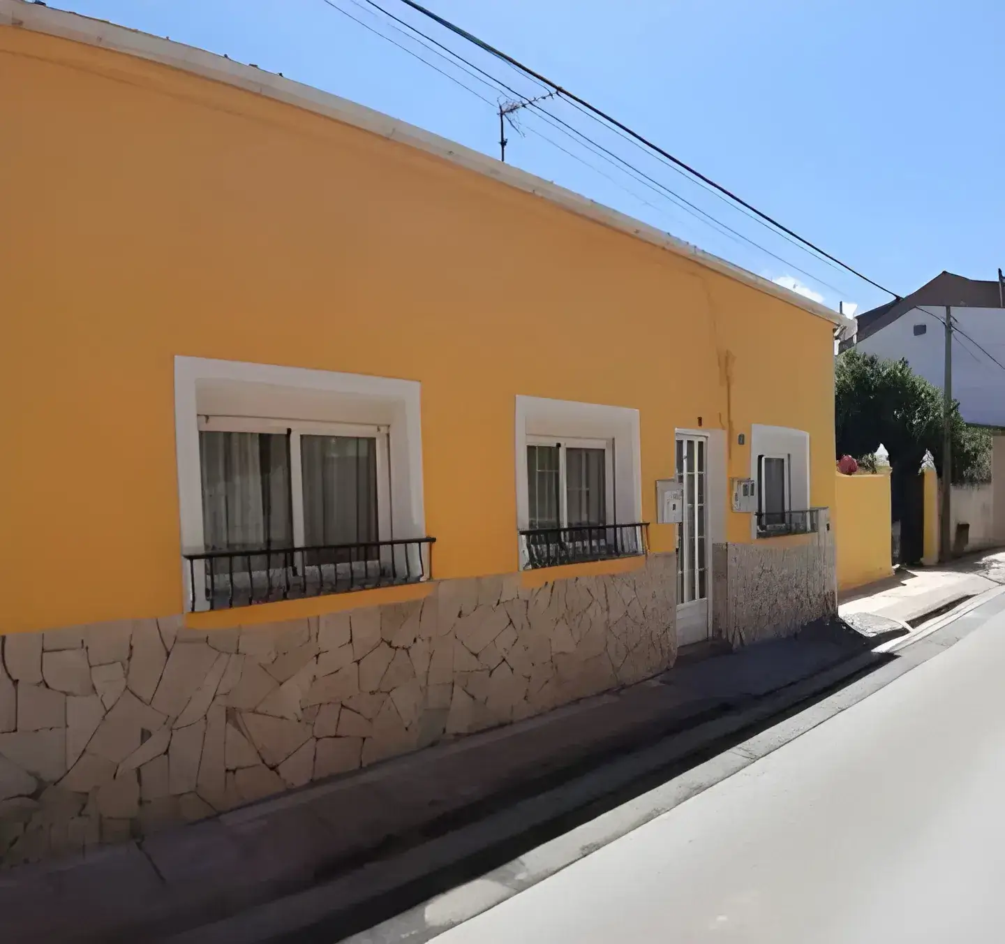 Los Pintores Badalona Fachada de casa tradicional pintada en color amarillo con zócalo de piedra
